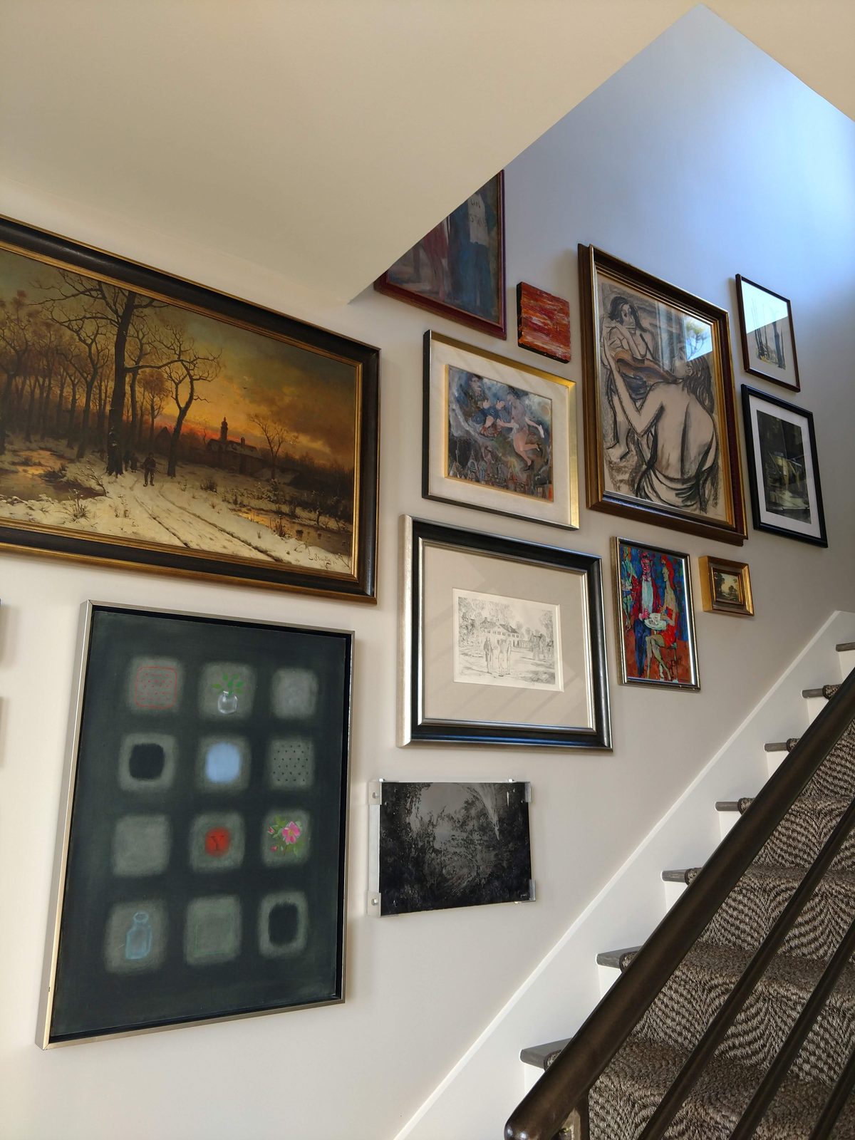 A gallery wall of custom-framed paintings, drawings and prints climbing a staircase in a client's home