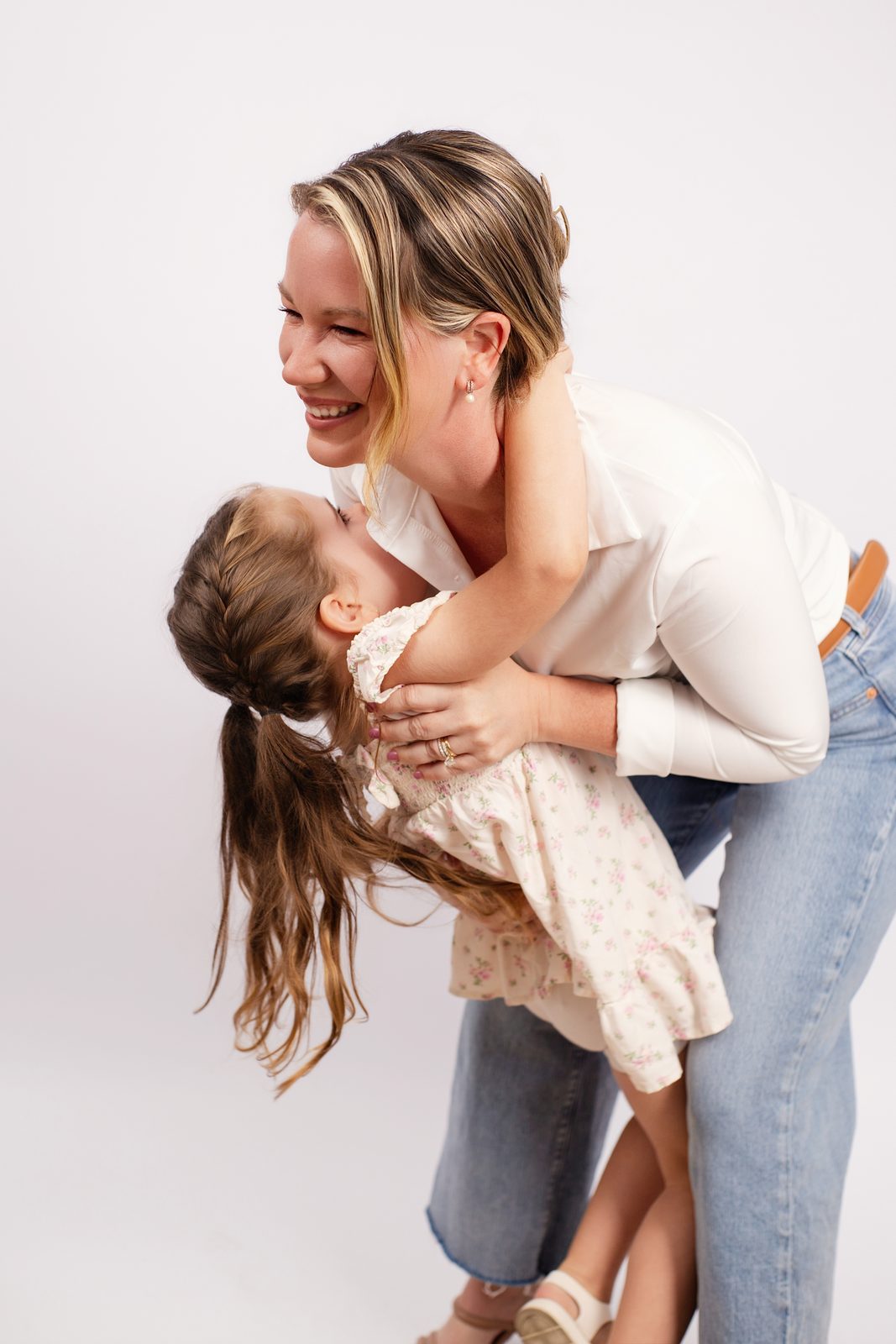 Angelina Creger laughing as she hugs her young daughter against a white studio backdrop
