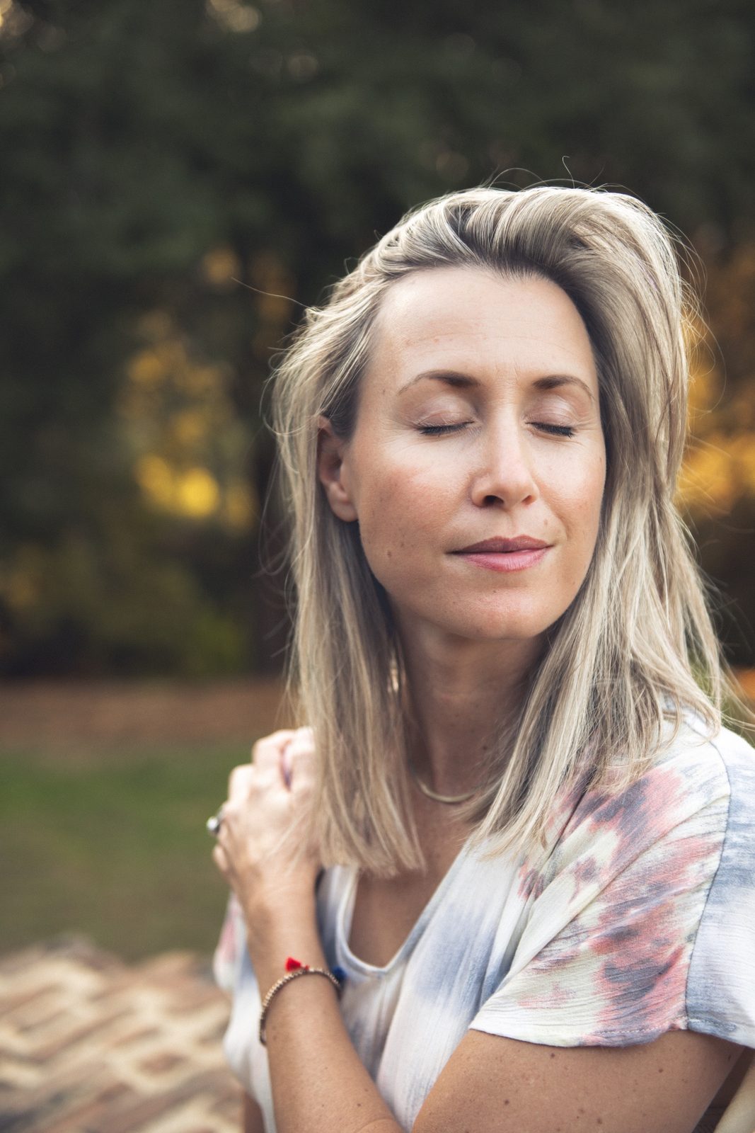Anna Christine Bowden, founder of In The Moment Anna, with her eyes closed and a hand resting on her shoulder, outdoors in soft golden light