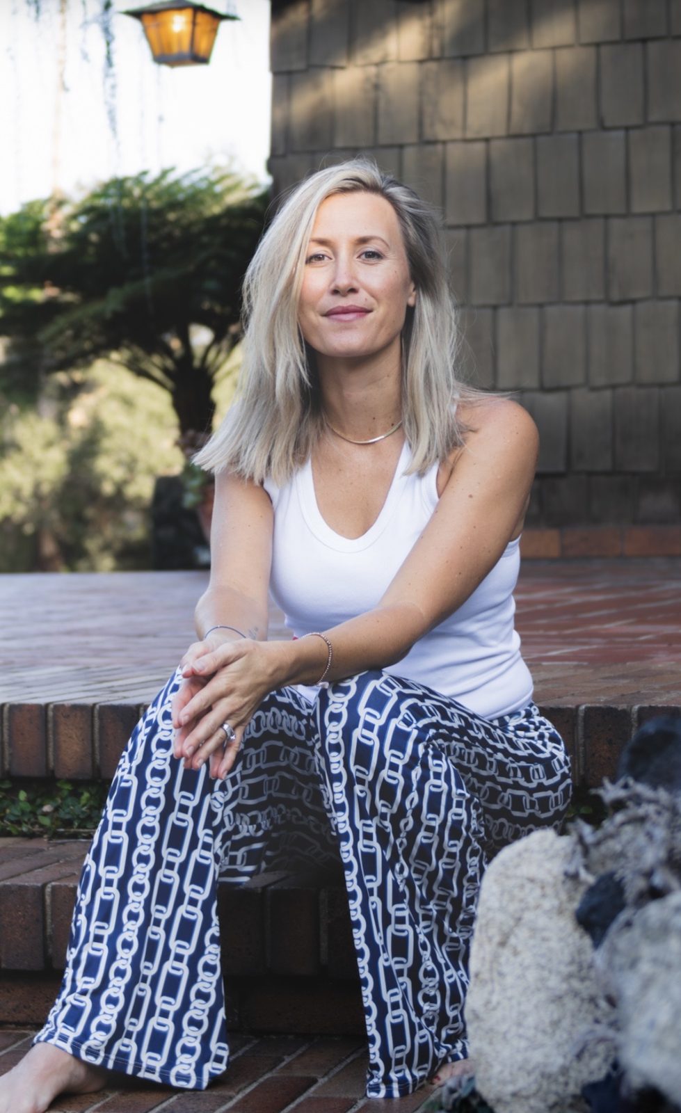 Anna Christine Bowden smiling on brick steps in a white tank top and patterned trousers