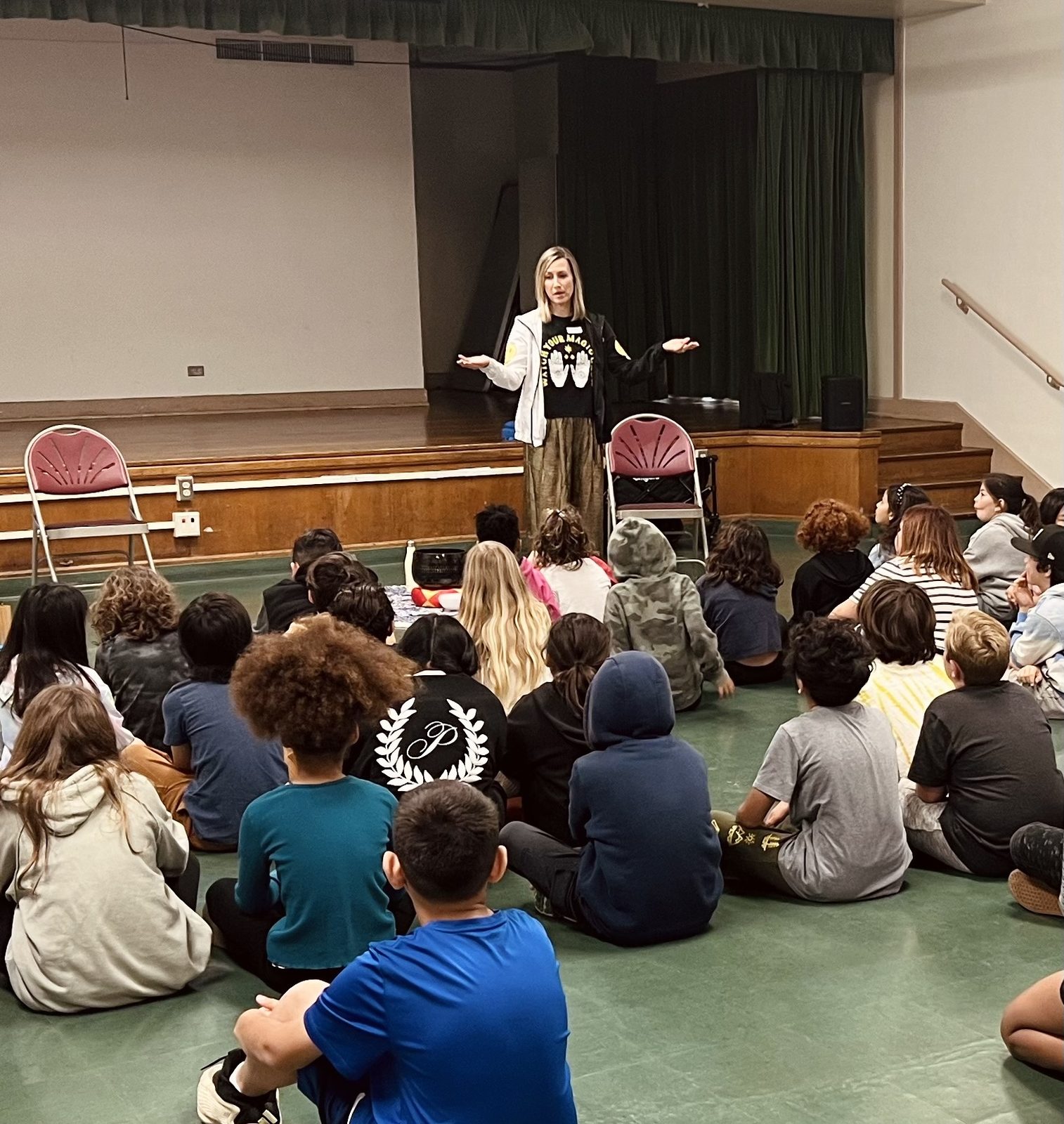 Anna Christine Bowden speaking to a room of seated elementary school students at a mindfulness assembly