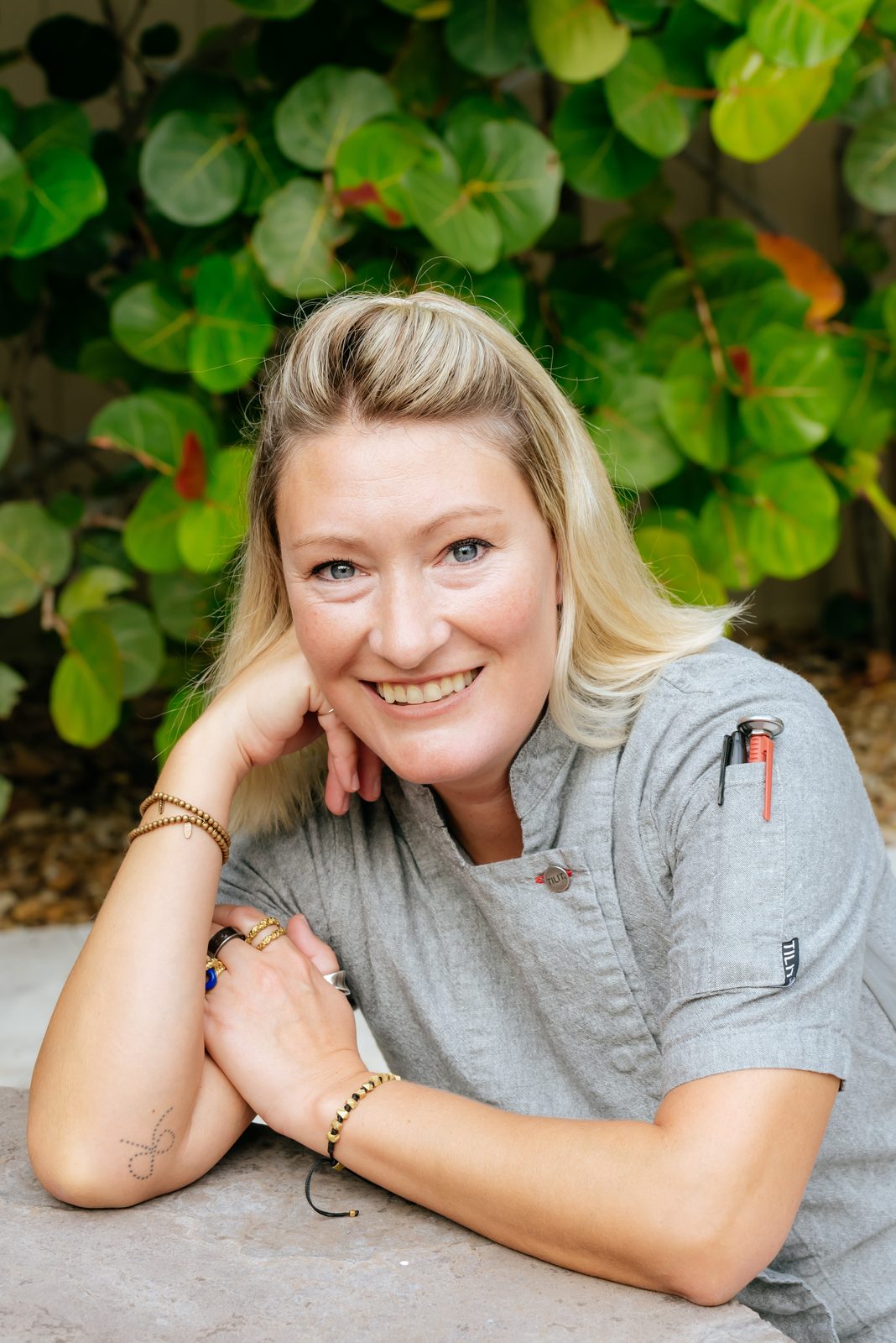 Ashley Ondrick, founder of A (Mostly) Healthy Chef, in a grey chef coat smiling in front of sea grape leaves