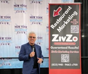 Benson J. Fischer holding a microphone beside a ZivZo Restaurant Marketing banner at the New York Restaurant Show