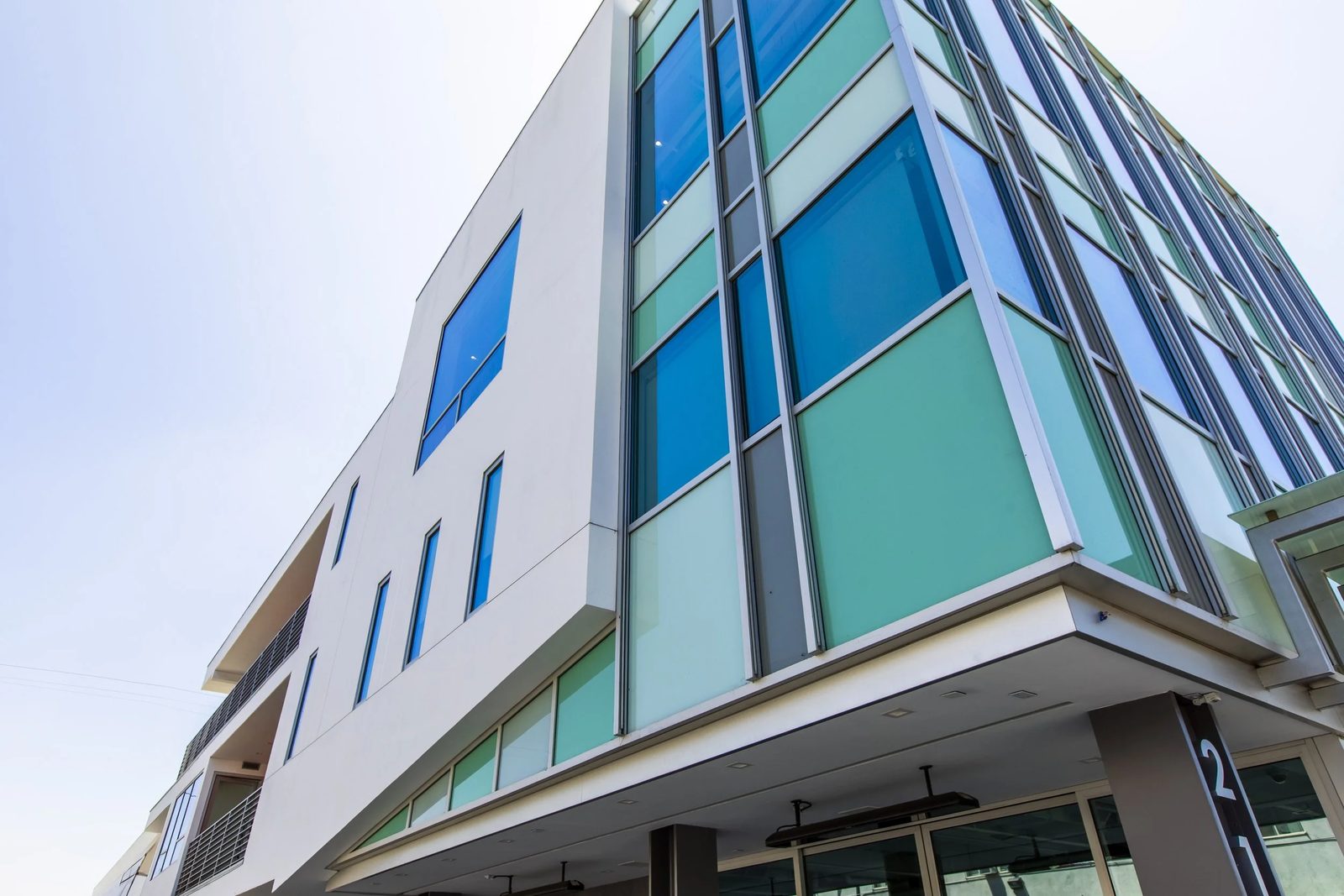 Modern multi-story building with a curved facade of glass windows in green and blue shades against a light sky.