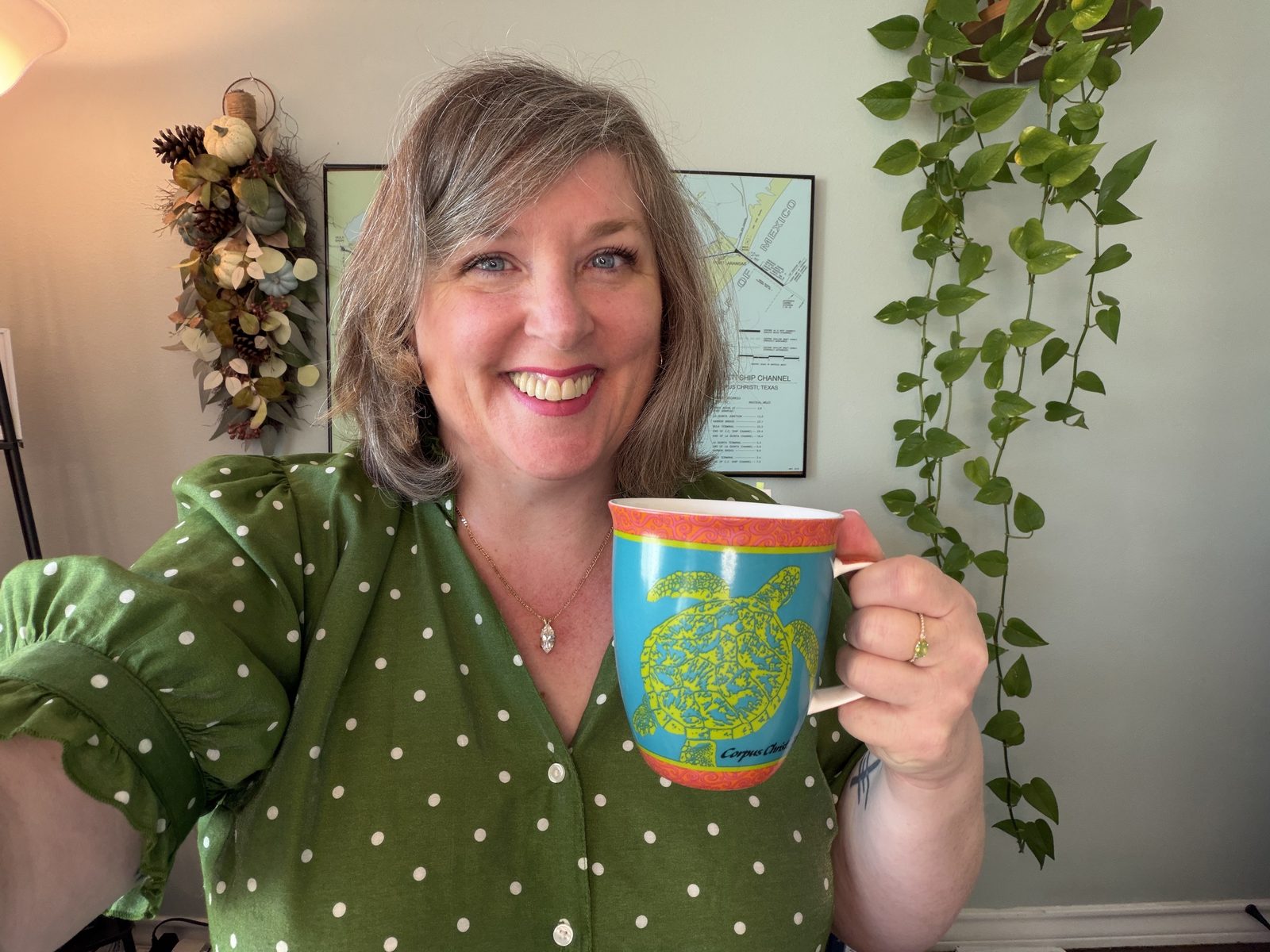 Bridget Willard, founder of Bridget Willard, LLC, smiling in a green polka-dot blouse and holding a Corpus Christi sea turtle mug