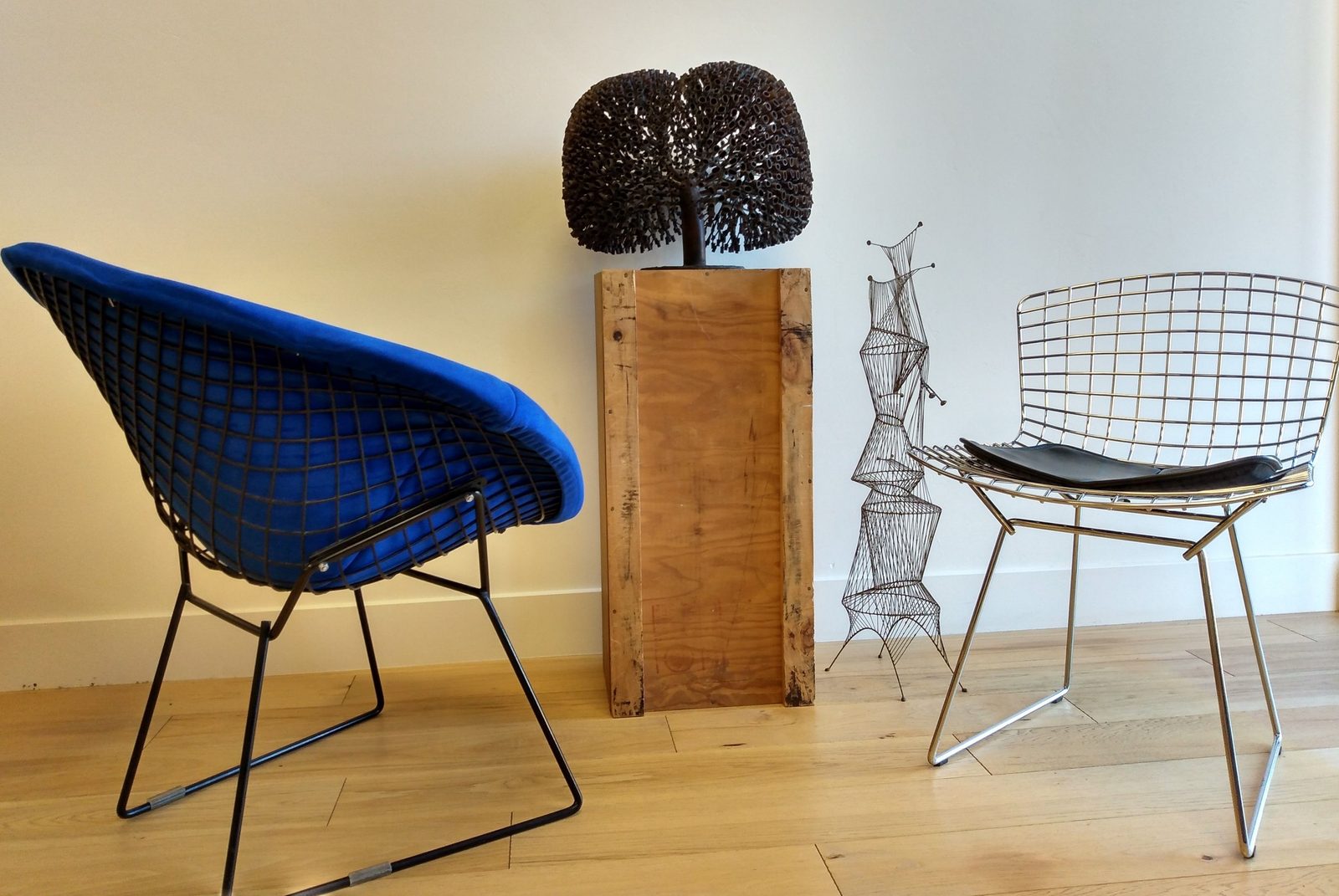 A blue Bertoia Diamond chair and a wire side chair beside Bertoia sculptures on wooden plinths in the Foundation gallery