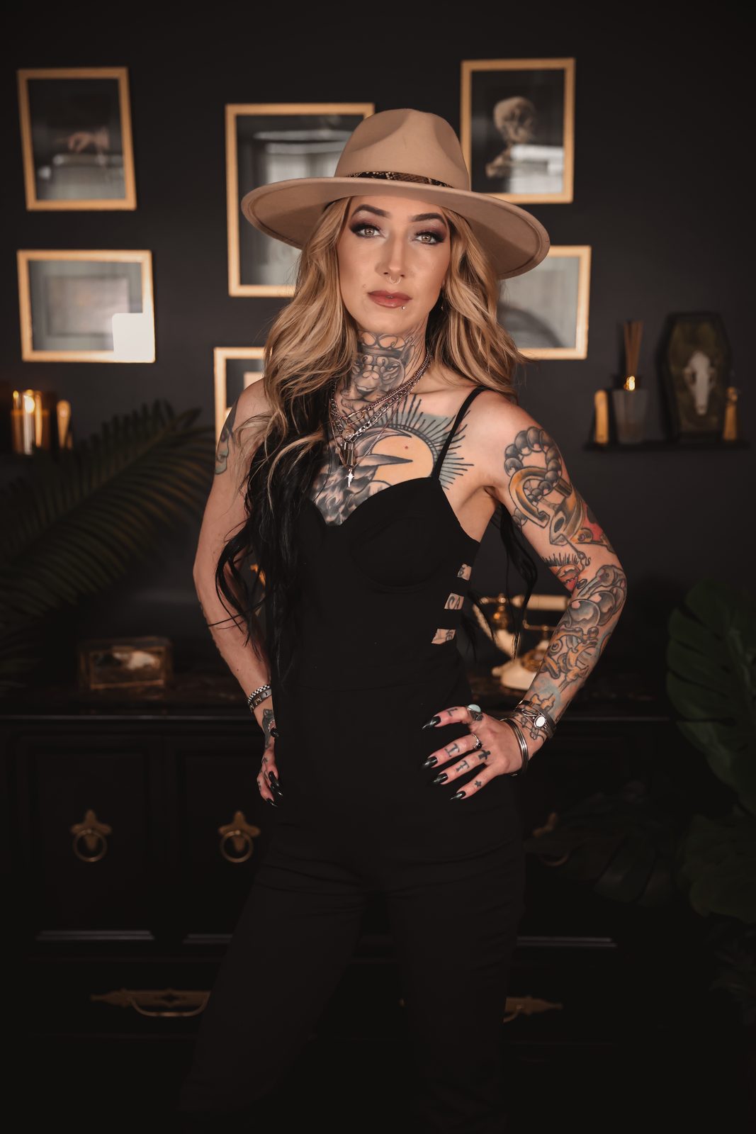 Chelsea Elle in a tan wide-brimmed hat and black jumpsuit, hands on her hips