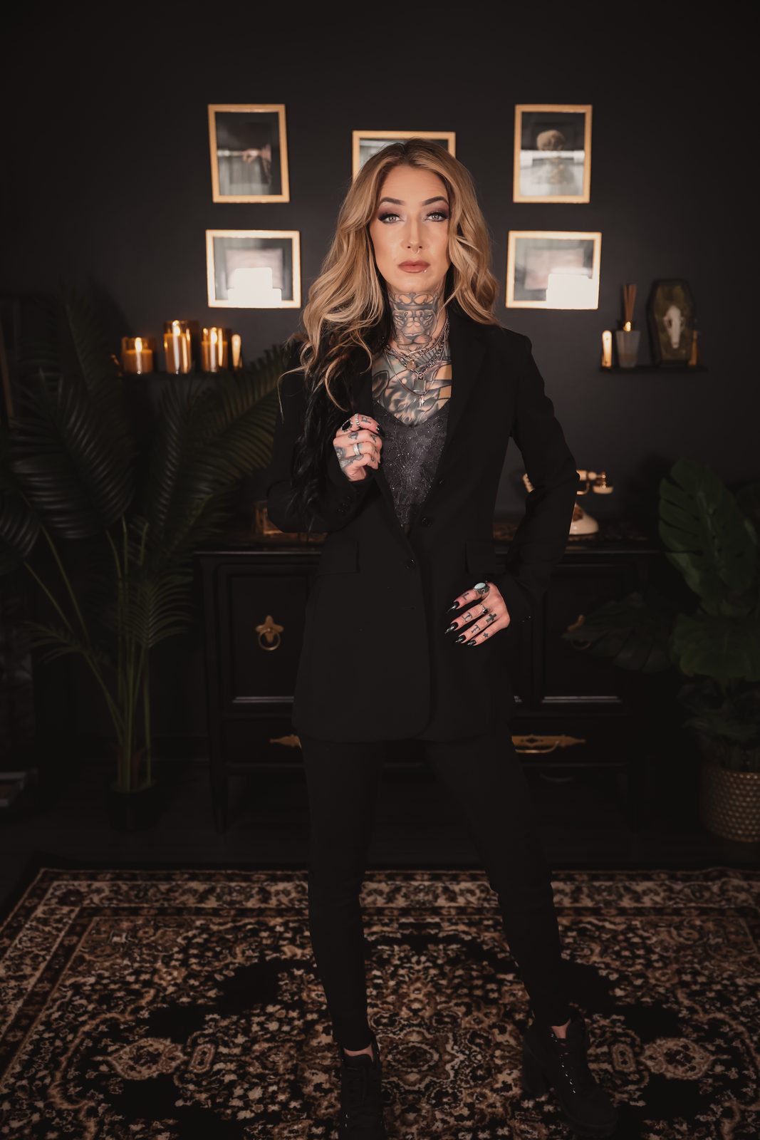 Chelsea Elle in a black blazer and jeans, standing on a patterned rug in a candle-lit room