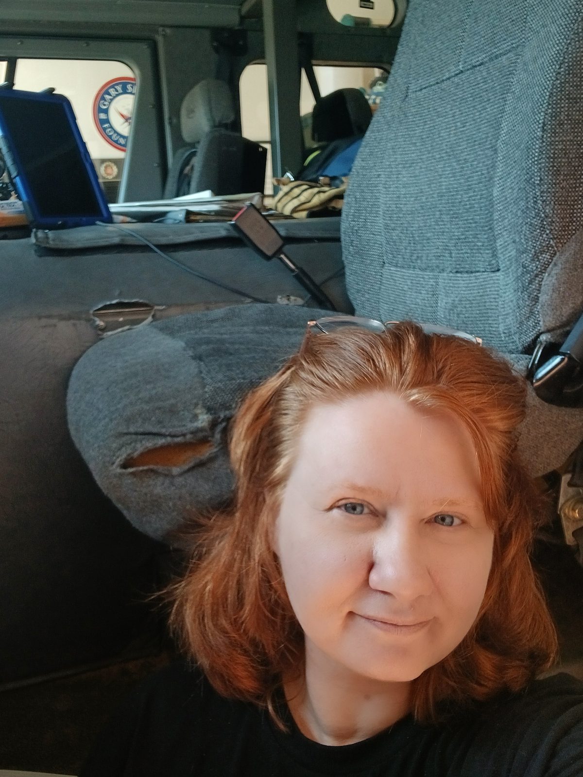 Christena Plummer inside a vehicle beside a worn grey cloth seat waiting to be reupholstered