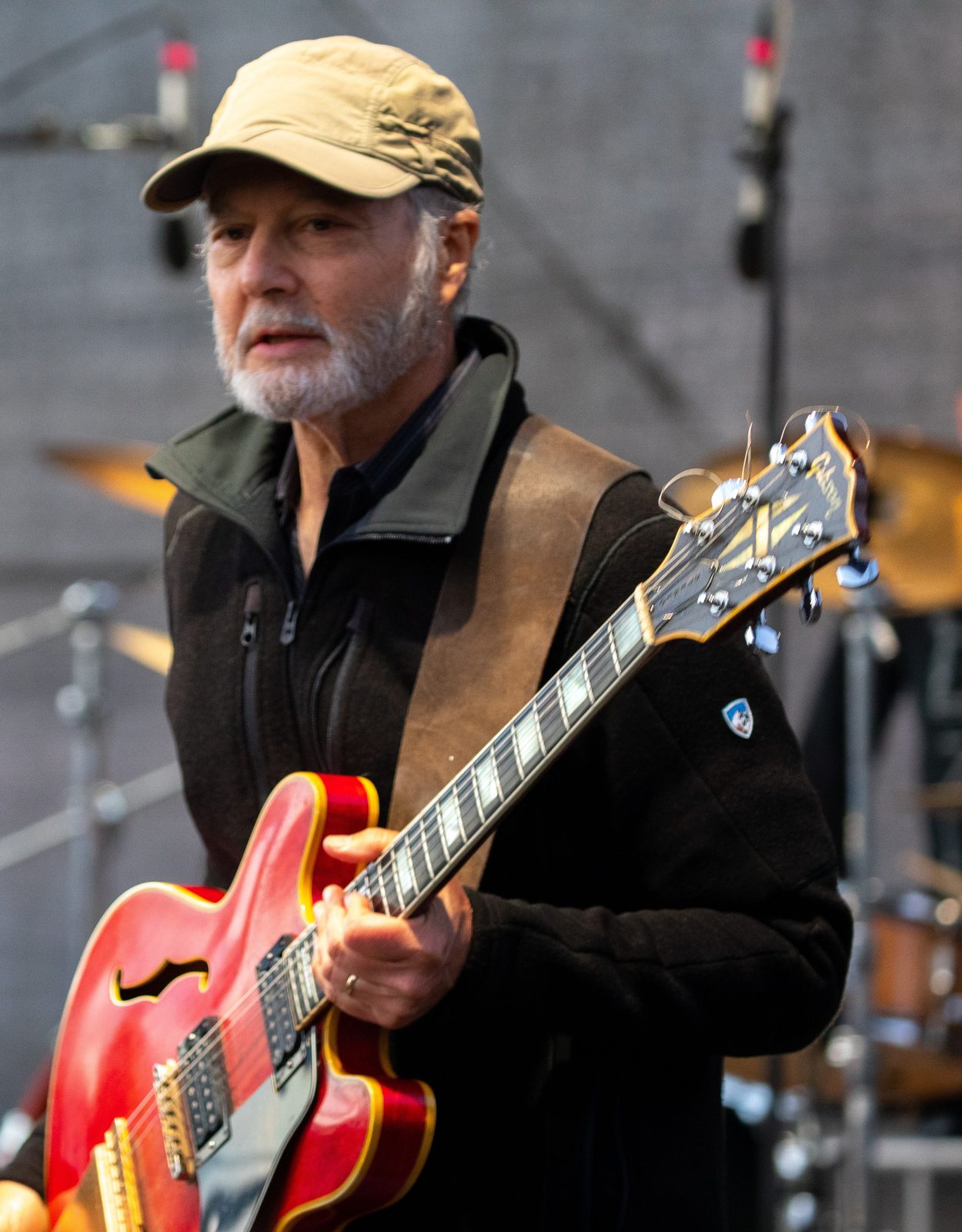 Dan Zalles, singer-songwriter and producer behind Dan Zalles Music, on stage in a khaki cap with a red Gibson semi-hollow guitar