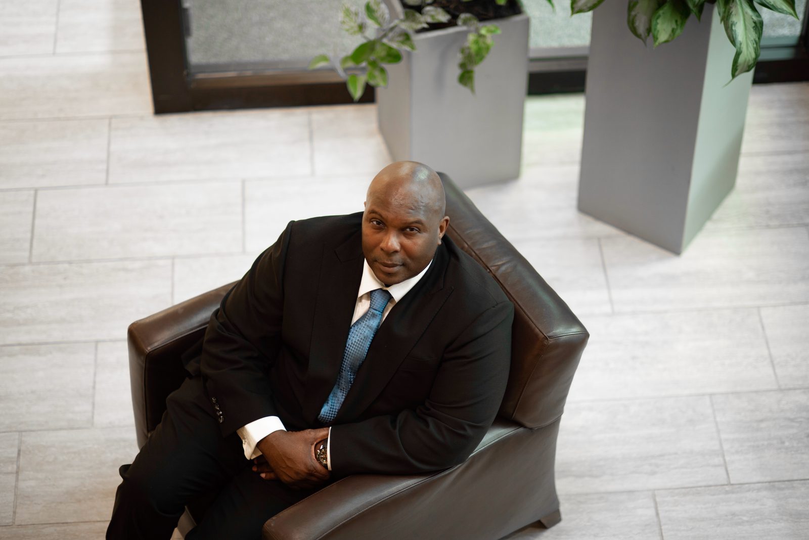 Devord J. Allen, founder of Breaking Barriers Inc., seated in a leather armchair in a suit and blue tie