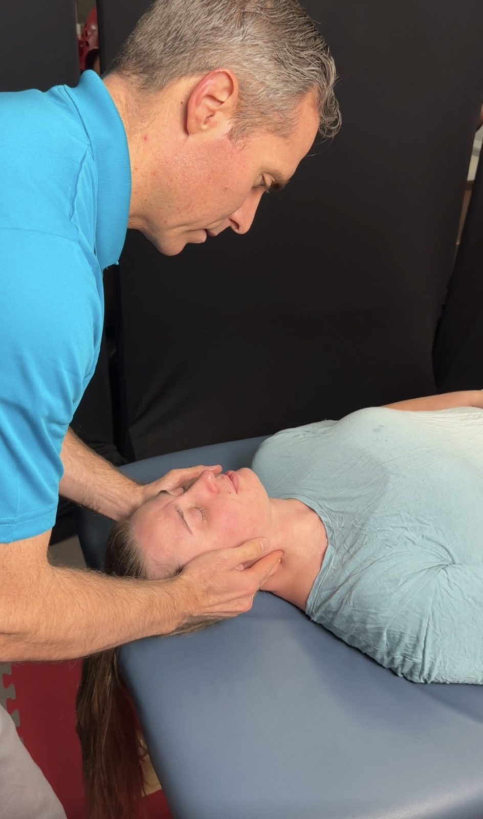 Dr. Doug Ashton gently treating a patient's neck as she lies on her back on a treatment table