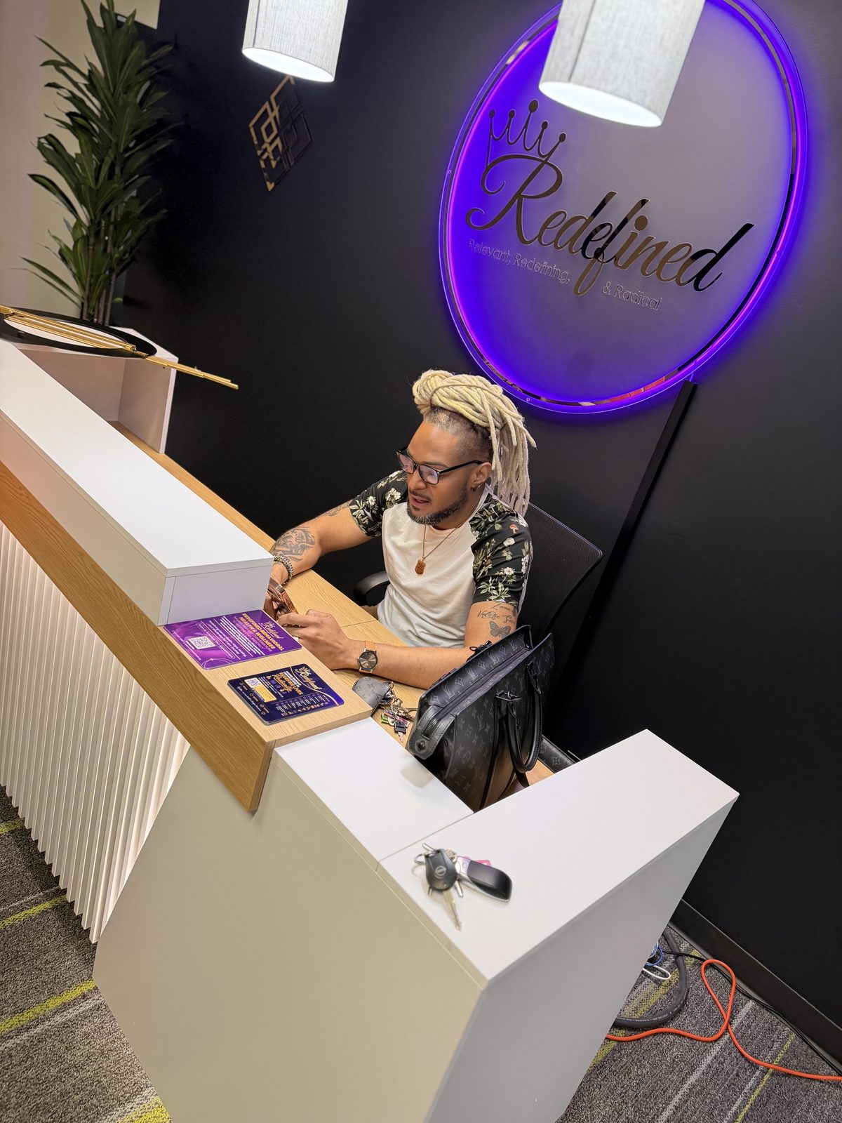 The Redefined reception desk under an illuminated purple Redefined sign