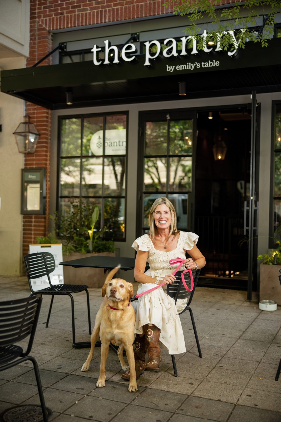 Emily Fournier seated with her yellow Labrador at a sidewalk table outside the Pantry by Emily’s Table in Greenville