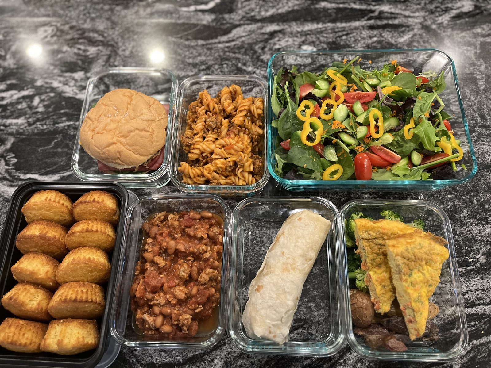 Glass containers of prepared meals by Chef Felicia, including salad, pasta, empanadas and a frittata