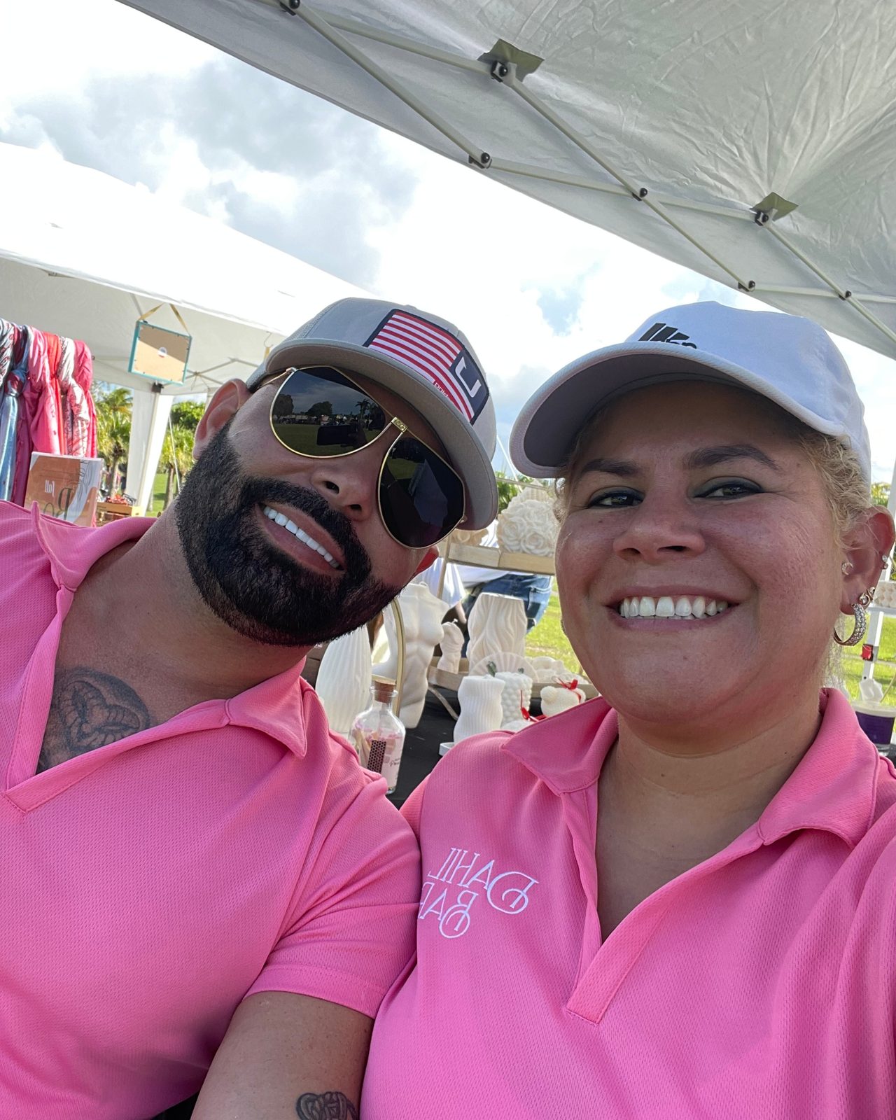 Hilda Rodriguez in a pink Dahil Bar polo at an outdoor market tent, with sculptural candles on the table behind her