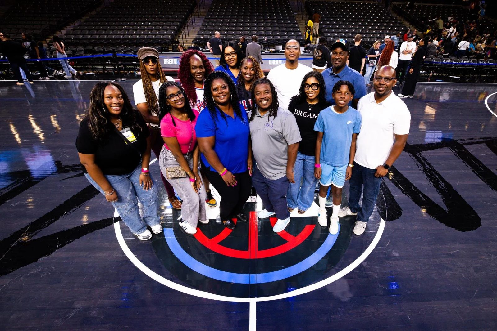 Group of people standing on a basketball court with a team logo, posing for a photo.