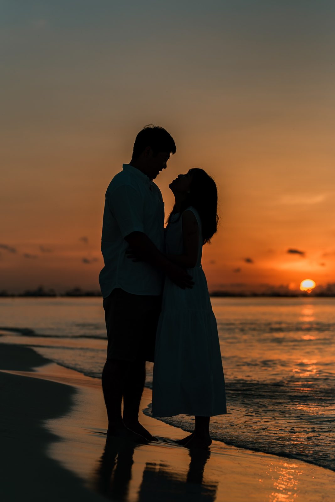 A couple silhouetted at sunset on the shoreline, photographed by Idaly Bustamante