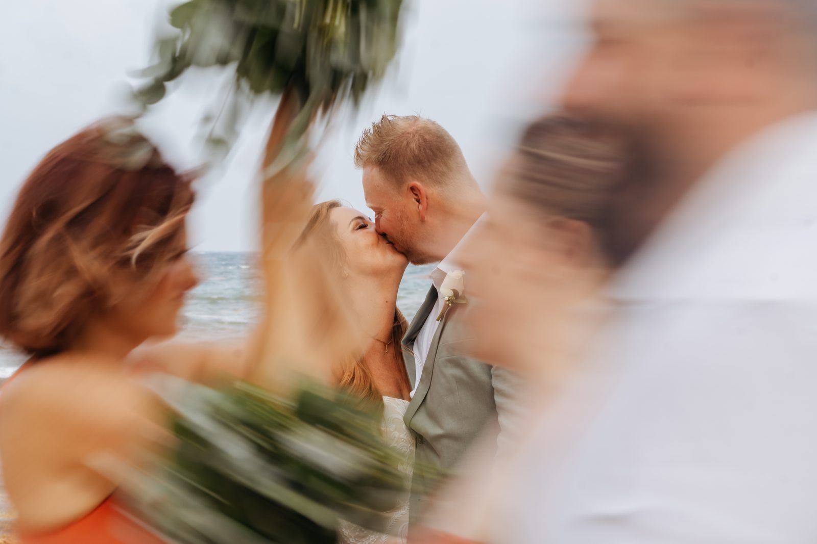 Newlyweds kissing as guests throw flowers at a beach wedding, photographed by Idaly Bustamante