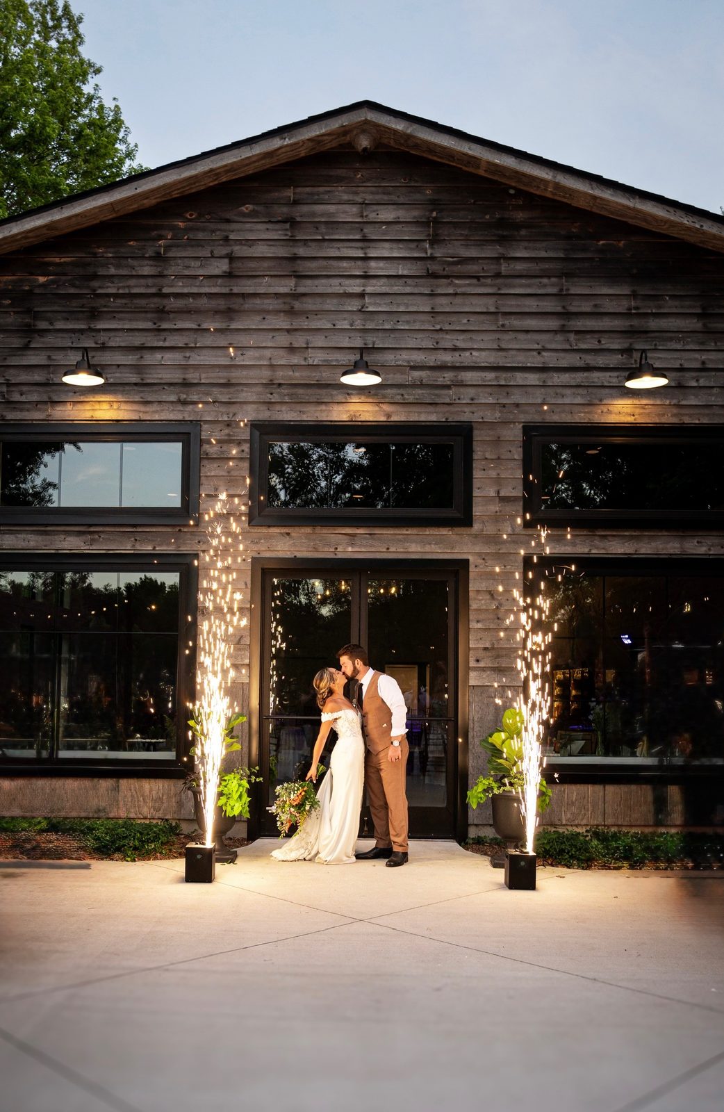 A newly married couple kissing outside the barn at Celestial Farms, framed by sparklers
