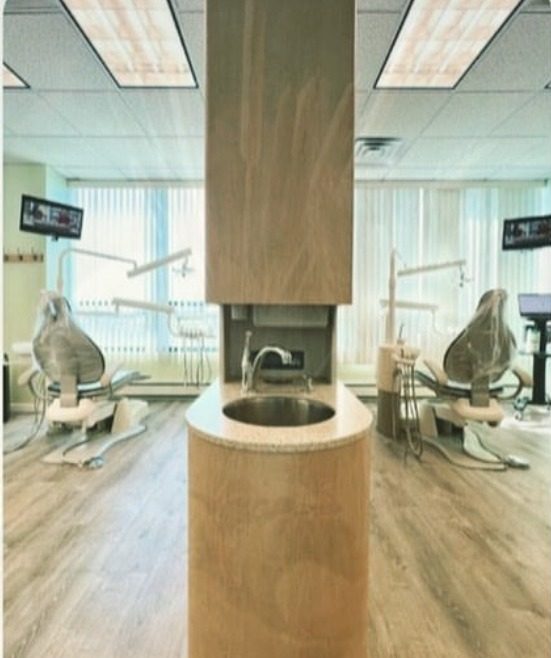 Two dental chairs either side of a wood-panelled sink column in a bright treatment room with wood floors