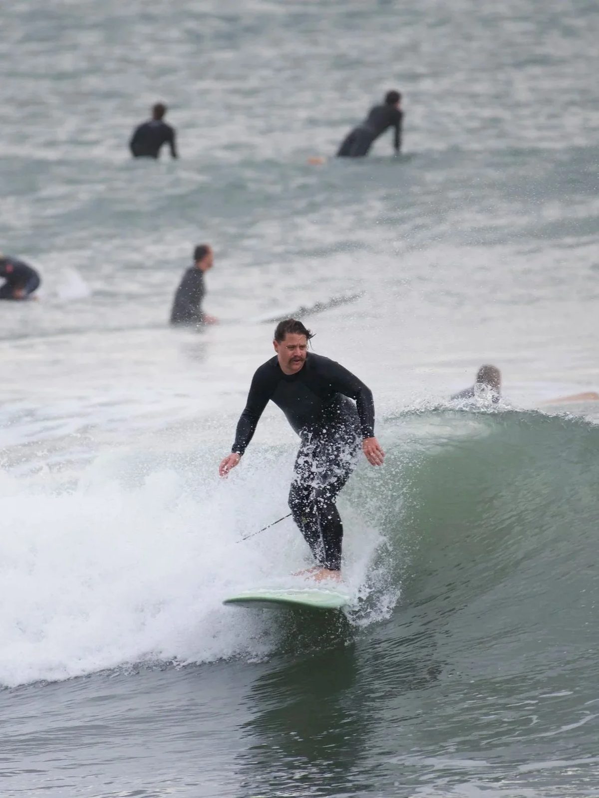 A man surfing on a wave in the ocean with several other surfers in the background.