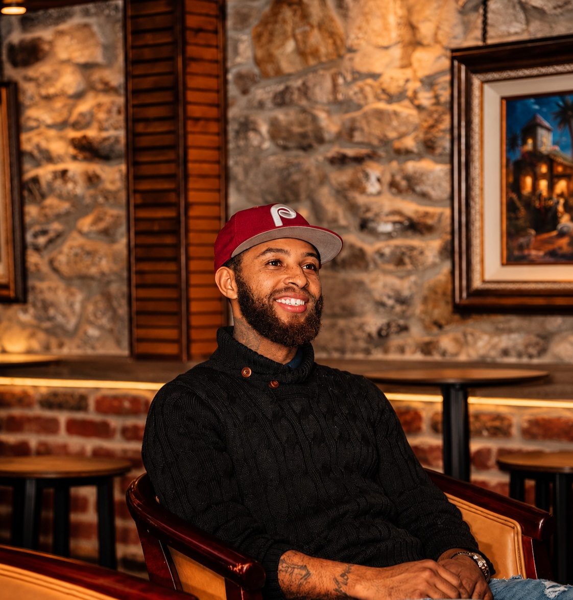 Joseph Thomas, known as Philly Joe, founder of Philly Joe Tattoo Studio in Newtown, Pennsylvania, smiling in a red Phillies cap and black sweater