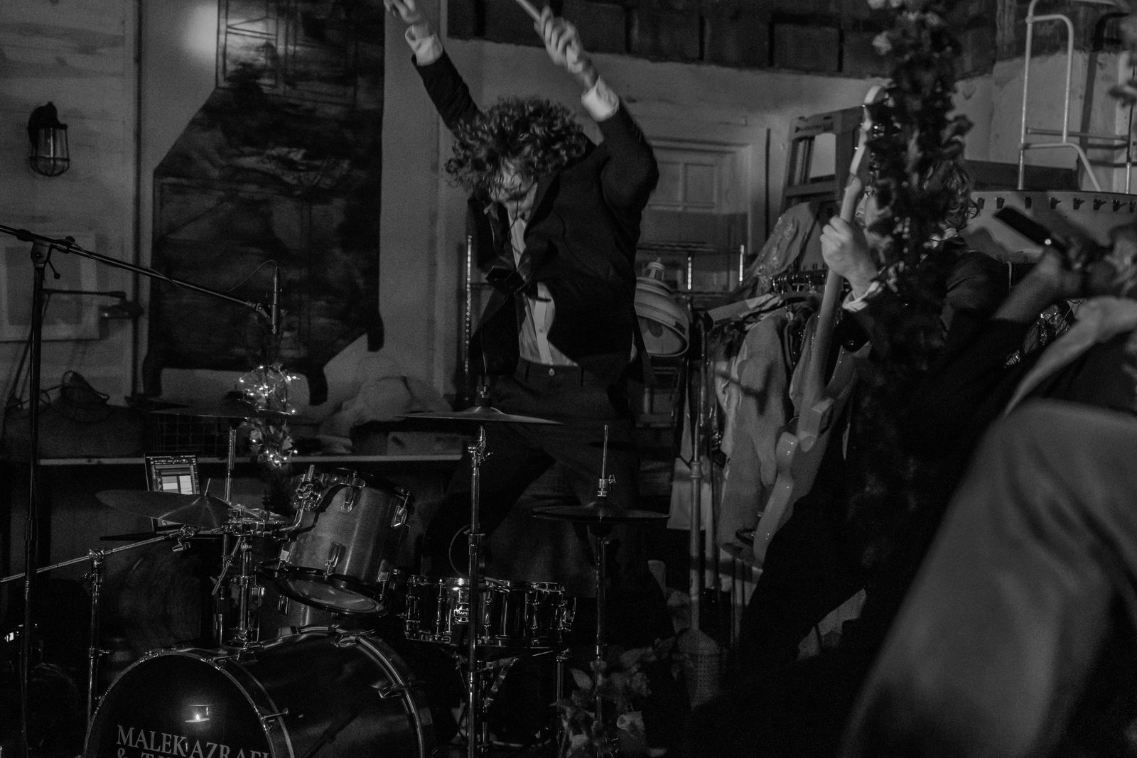 Josh Luke mid-performance behind the drum kit at a Malek and the Vibez show, sticks raised