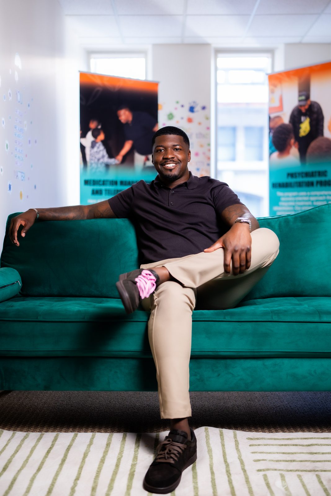 Karahn Alston seated on a teal sofa at the clinic, with banners for medication management and the psychiatric rehabilitation program behind him