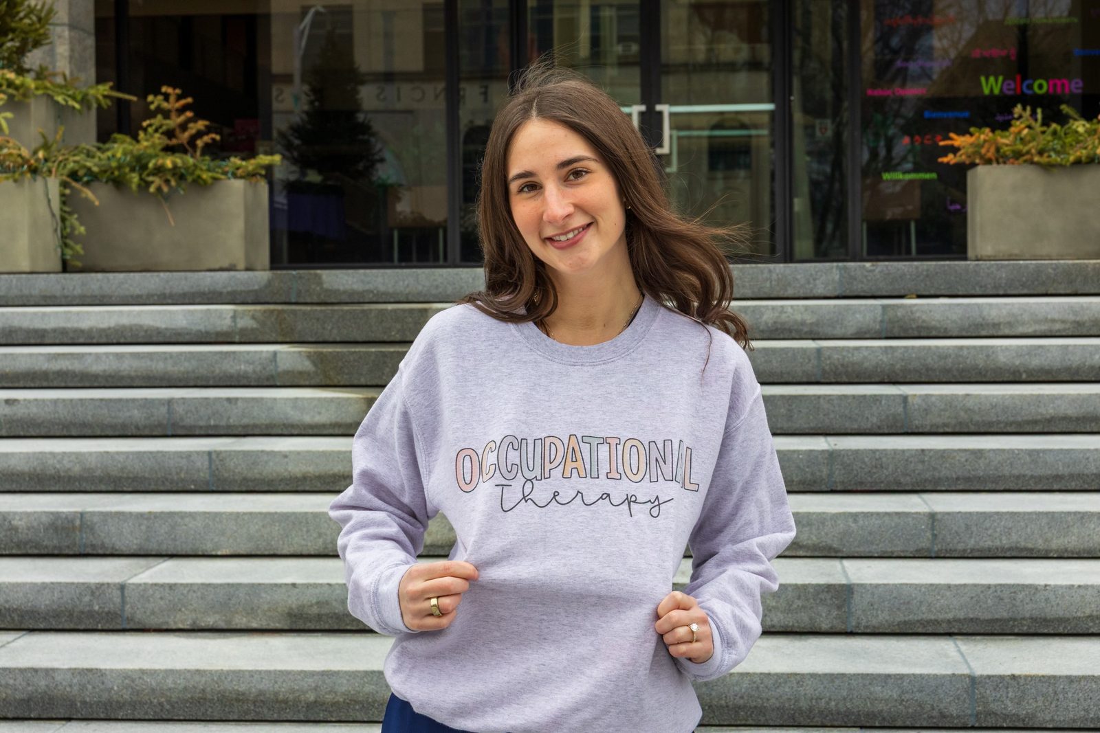 Kristen Sellars, the occupational therapist behind OT Insider, smiling in an Occupational Therapy sweatshirt on a flight of stone steps