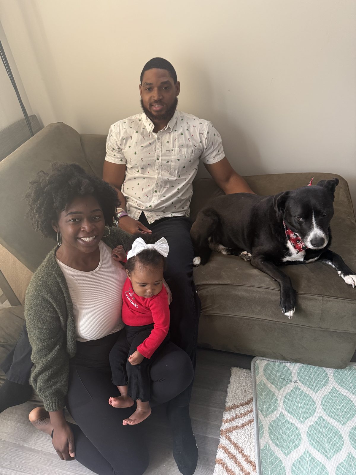 Lance and Monica Felder at home with their daughter on Monica’s lap and a black dog on the couch