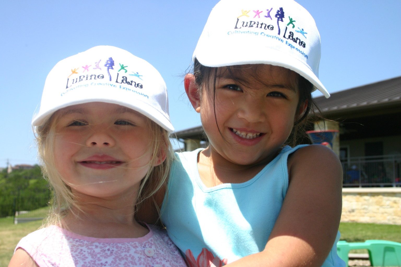 Two Lupine Lane students in white Lupine Lane caps smiling in the sun