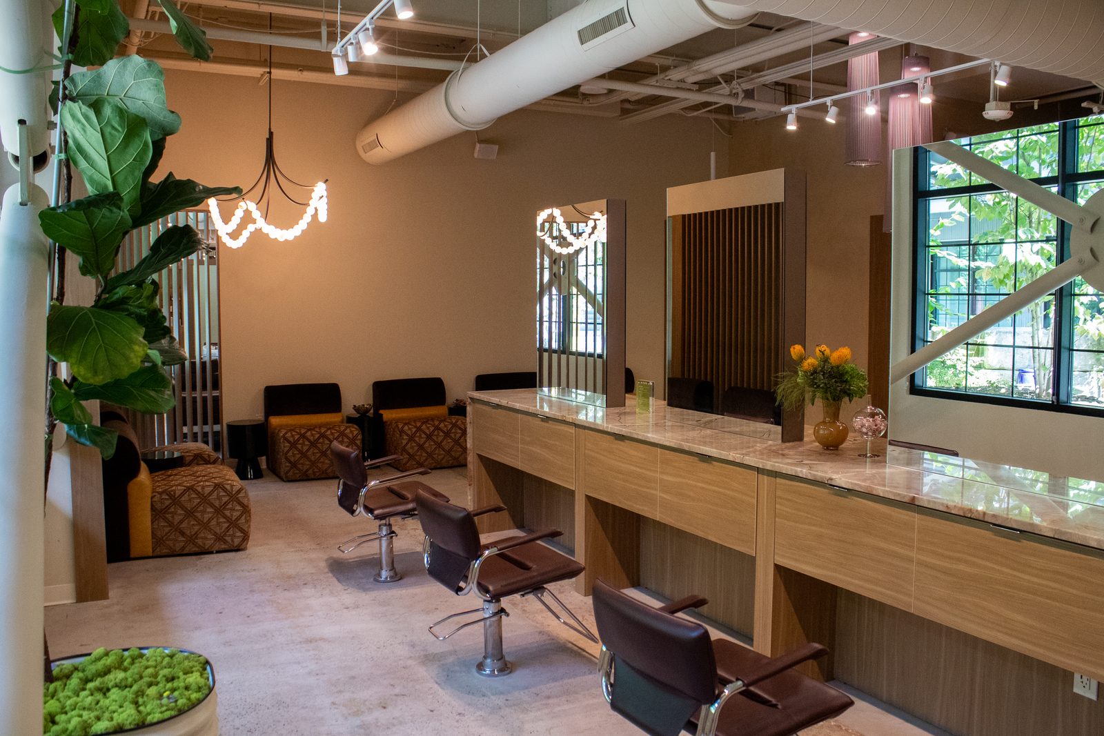Styling stations with marble counters, leather chairs and framed mirrors on the salon floor at Sunday Salon