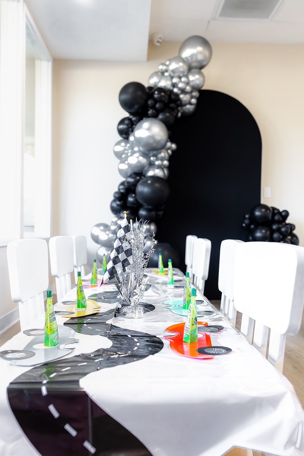 A race-car themed birthday table at Coastal Kids Playspace with a road-print runner, checkered-flag centrepiece and a black and silver balloon arch