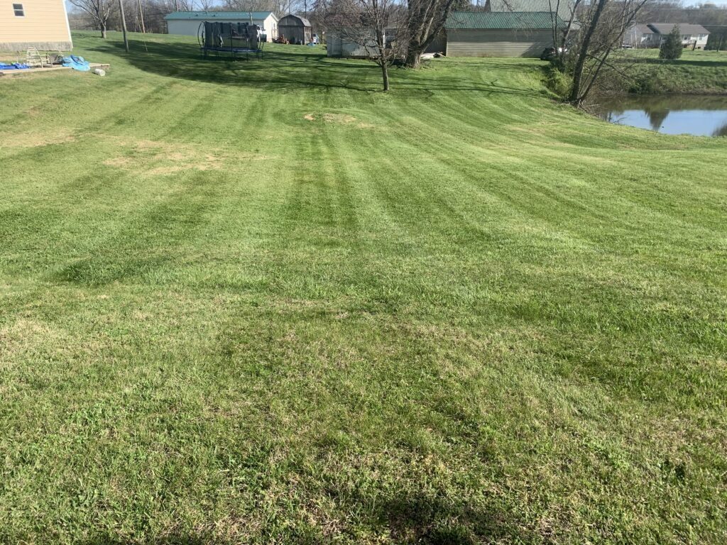 A commercial stand-on mower parked on a freshly striped lawn