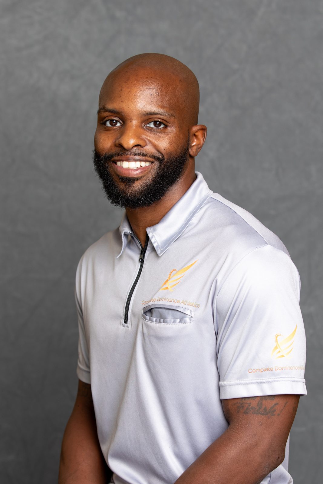 Milton Putman, founder and CEO of Complete Dominance Athletics, smiling in a grey CDA polo against a grey studio backdrop