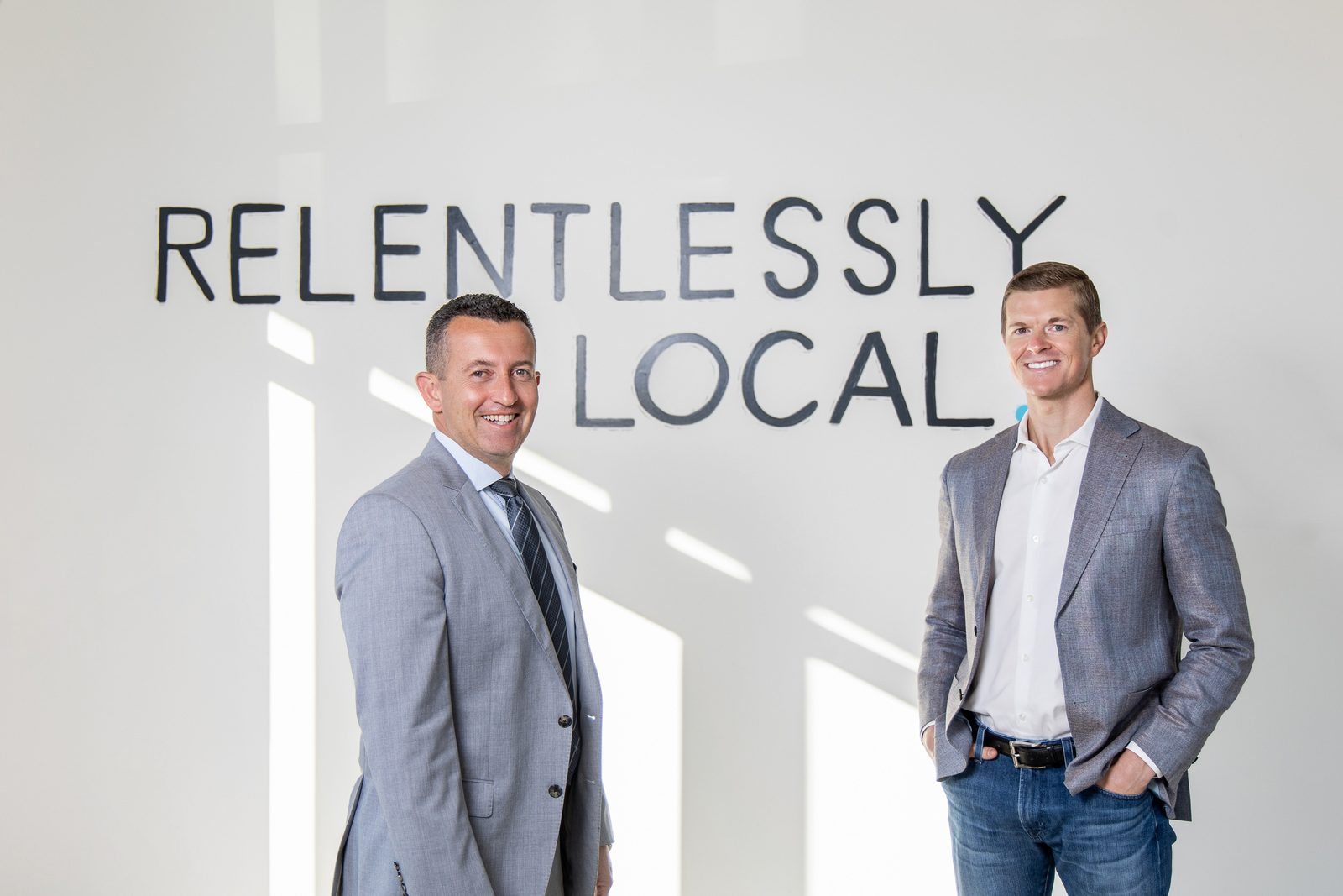 Oleg Bortman, left, and Tucker Blalock standing in front of a wall painted with the words Relentlessly Local