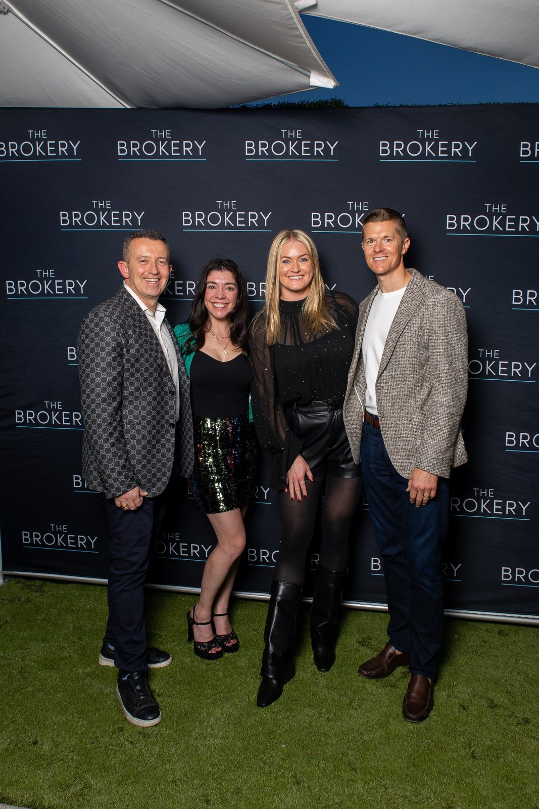 Oleg Bortman and Tucker Blalock with two colleagues in front of a The Brokery step-and-repeat backdrop at the company holiday party