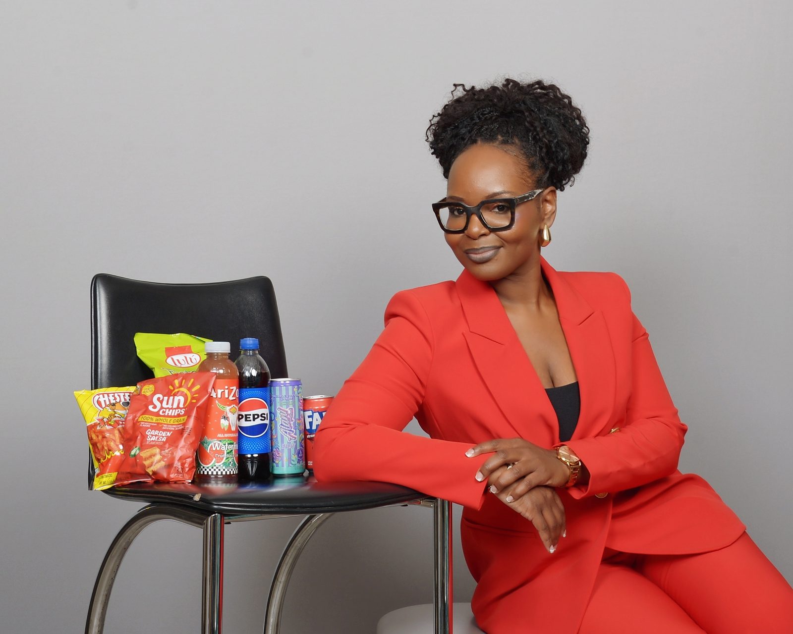 Priscilla Peete leaning on a chair stacked with the snacks and drinks Peete Vending stocks, including Sun Chips, Chester's, Arizona tea and Pepsi