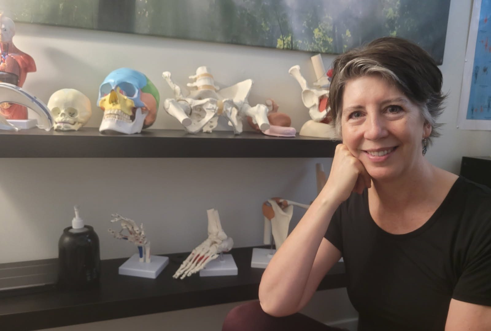 Rachel Tobler seated beside a shelf of anatomical models, including skulls, a pelvis, a foot and a hand