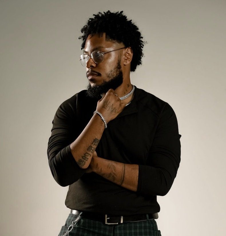 Remy Janvier, founder of JanviFX Studios, in a black long-sleeve top and wire-rimmed glasses, looking to the side with a hand at his collar