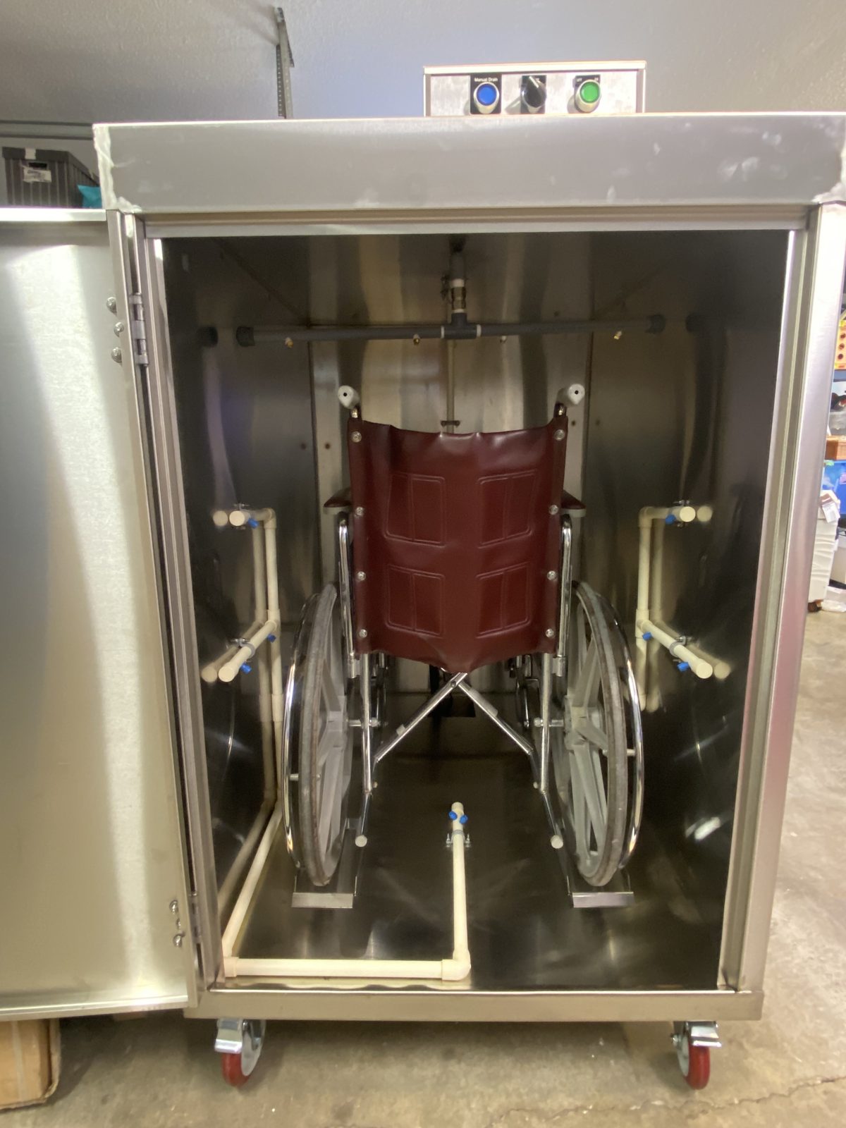 A wheelchair inside an open WeCare Solutions stainless steel wash cabinet
