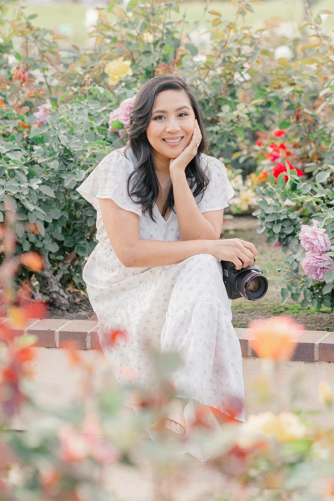 Sarom Thompson, San Diego family photographer, smiling in a rose garden with her camera