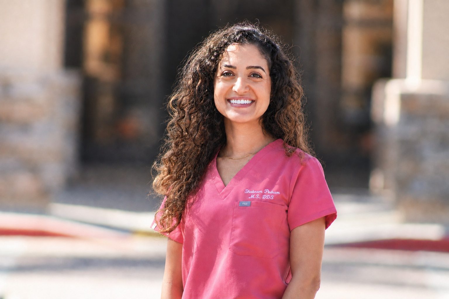 Shabnam Pedram Scott, DDS, co-owner of Gentle Dentistry of Poway, smiling in pink scrubs outside the practice in Poway, California