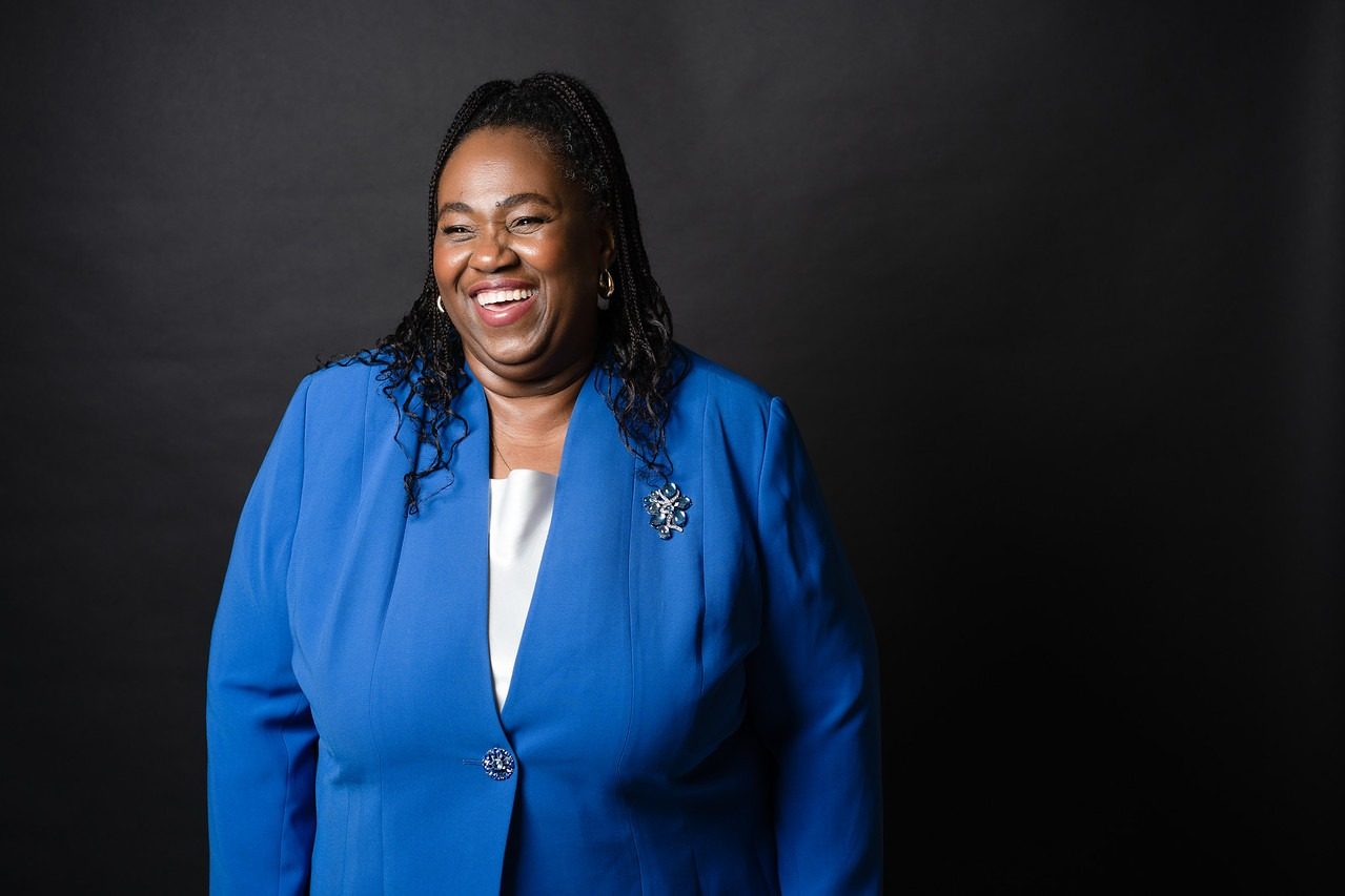 Dr. Sharon M. Jones laughing in a royal blue jacket against a black studio backdrop