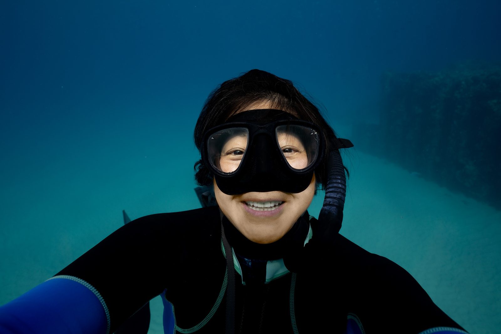 Shera Mercer, founder of ʻAlohi Kai, smiling underwater in a dive mask and wetsuit