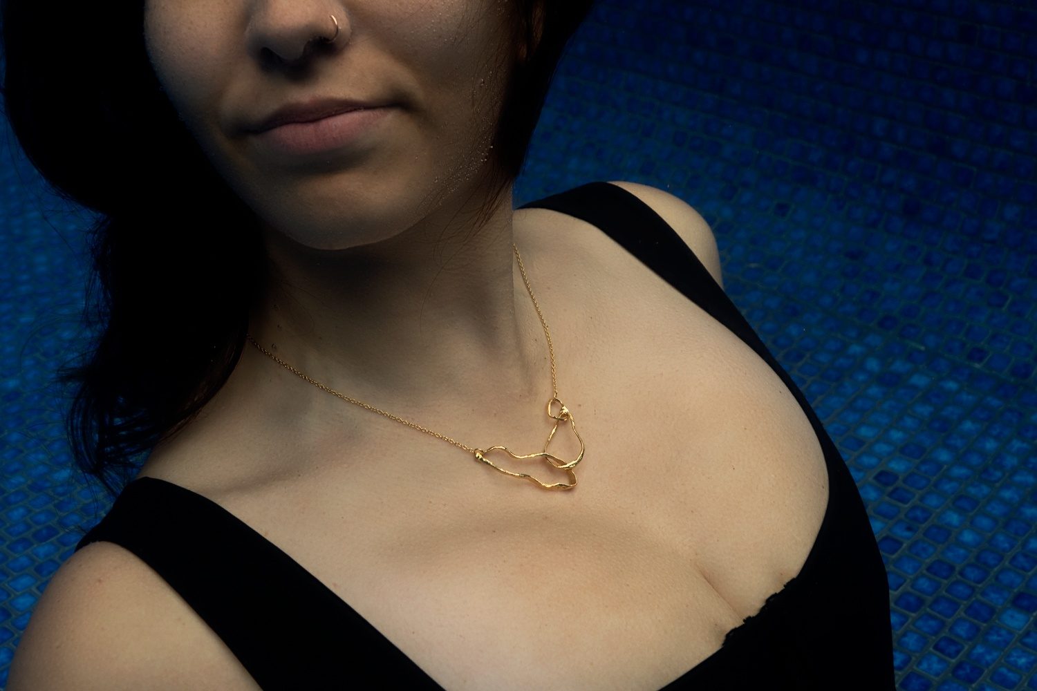 A gold ʻAlohi Kai marine-life necklace worn underwater against a blue tiled pool