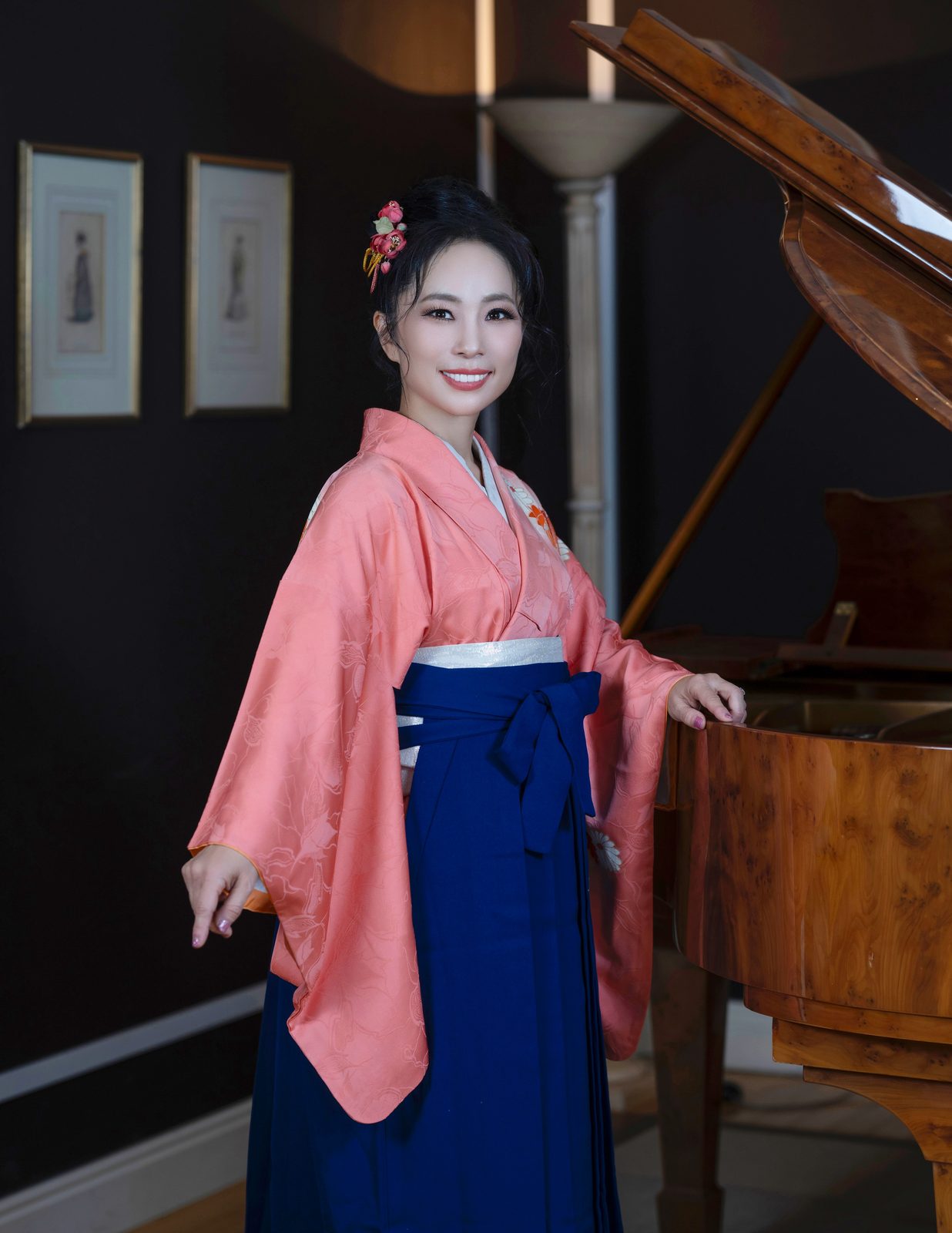 Shiho Brenner in a coral kimono and navy hakama, full length, with one hand resting on a grand piano