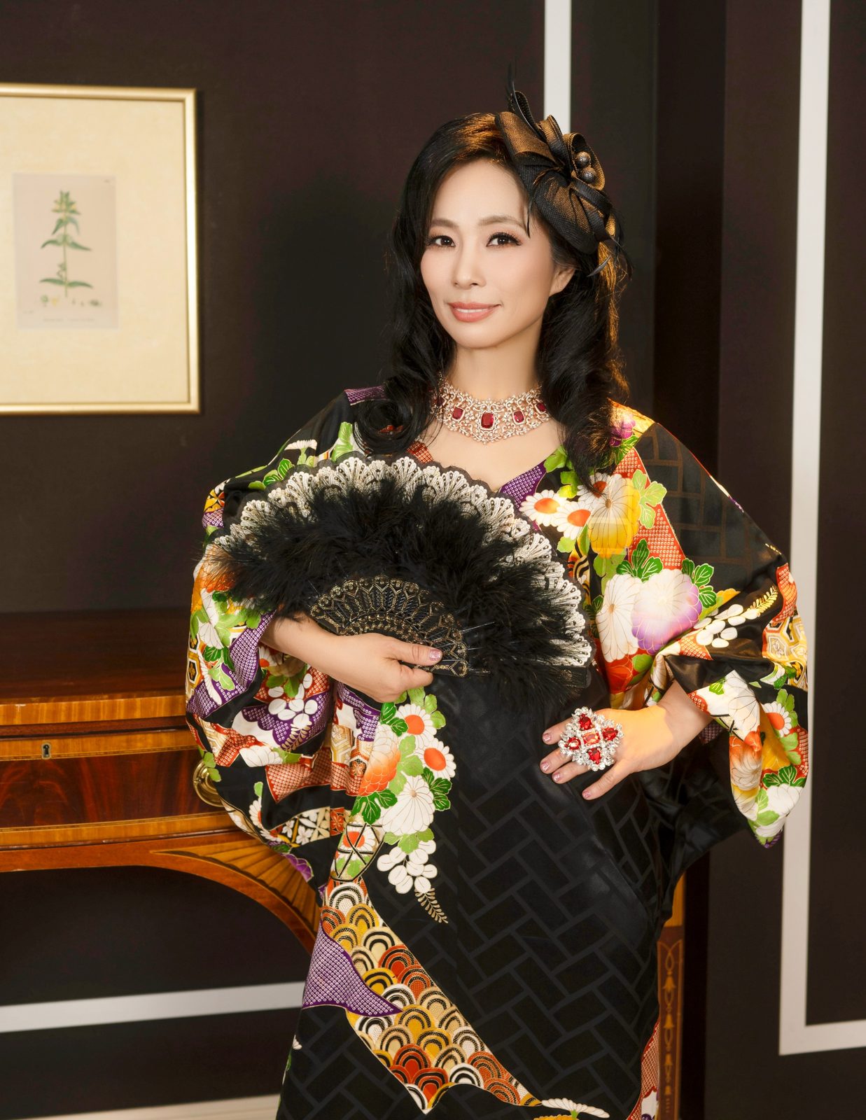 Shiho Brenner in a black floral kimono and fascinator, holding a black feather fan