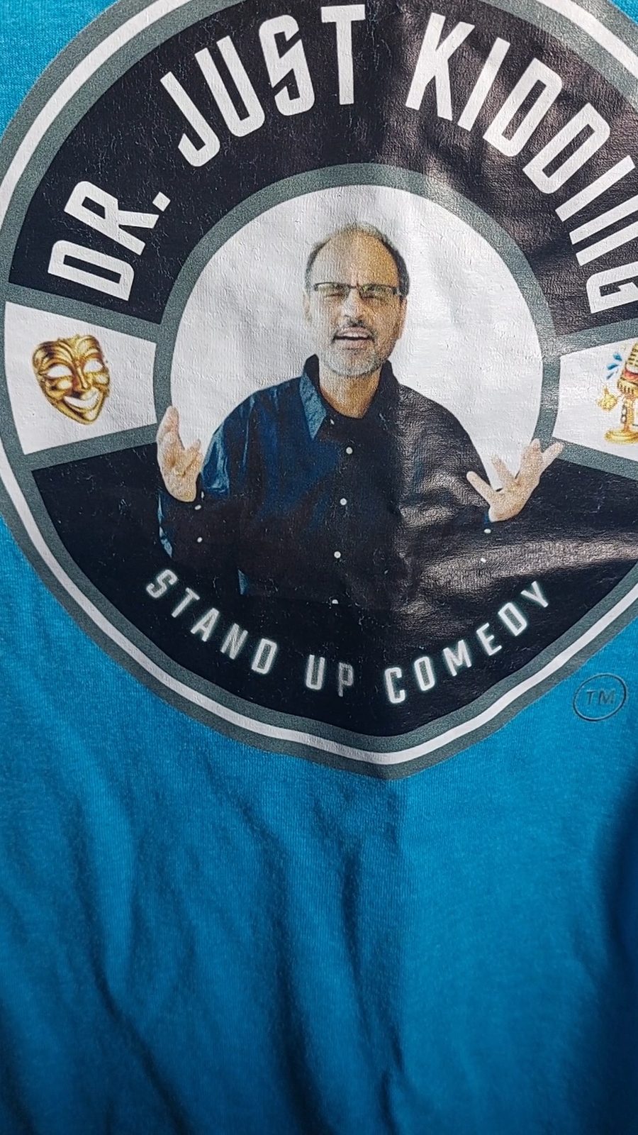 Dr. Just Kidding Stand Up Comedy emblem printed on a teal T-shirt, with a portrait of Sri, a comedy mask and a microphone